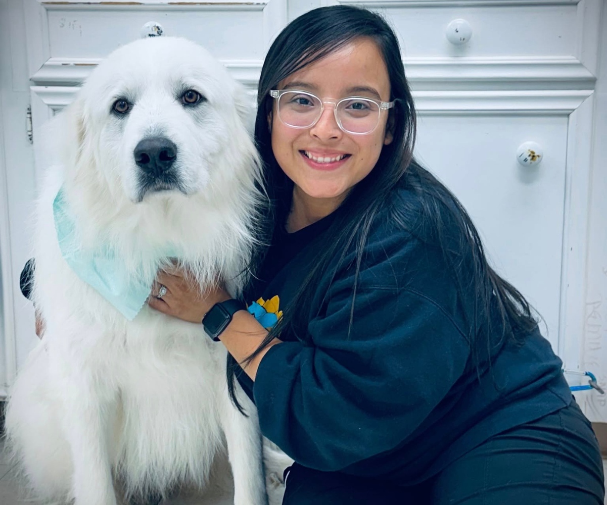 vet smiling and kneeling beside a large, fluffy white dog
