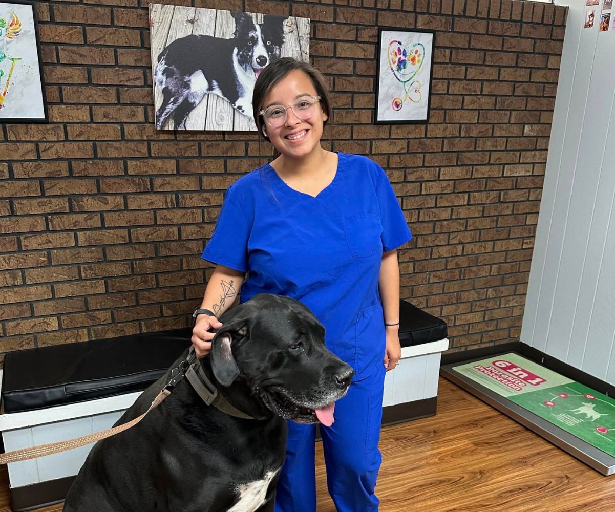 A woman in scrubs stands beside a large dog